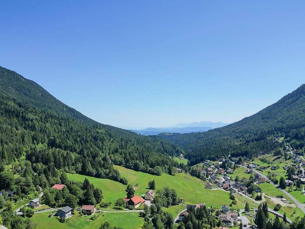 Weitläufiger Ausblick über ein idyllisches Tal mit kleinen Häusern und dichten Wäldern bis zum Horizont.