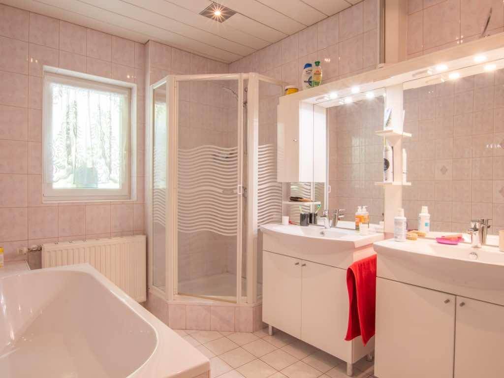 Geräumiges Badezimmer mit hellrosa Fliesen, Badewanne, Dusche und Doppelwaschbecken.