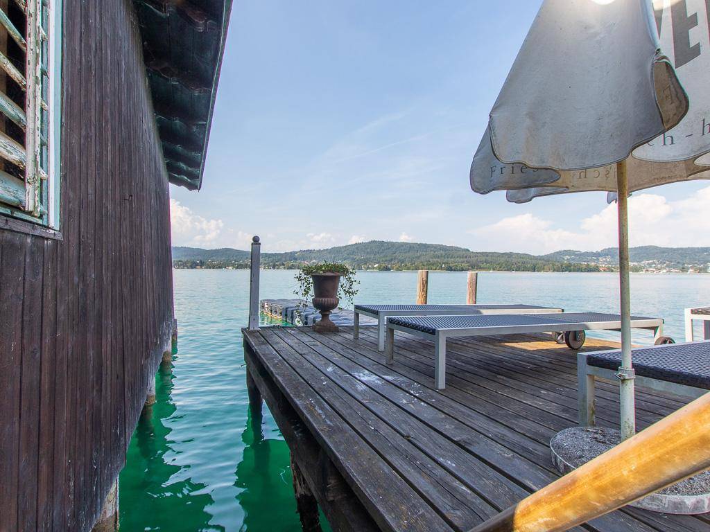 Holzterrasse am See mit Sonnenliegen, Sonnenschirm und weitem Blick auf die umliegende Natur.