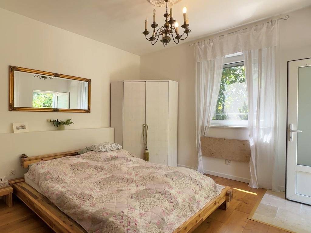 Schlafzimmer mit Holzbett, großem Spiegel und hellem Holzboden, gut beleuchtet.
