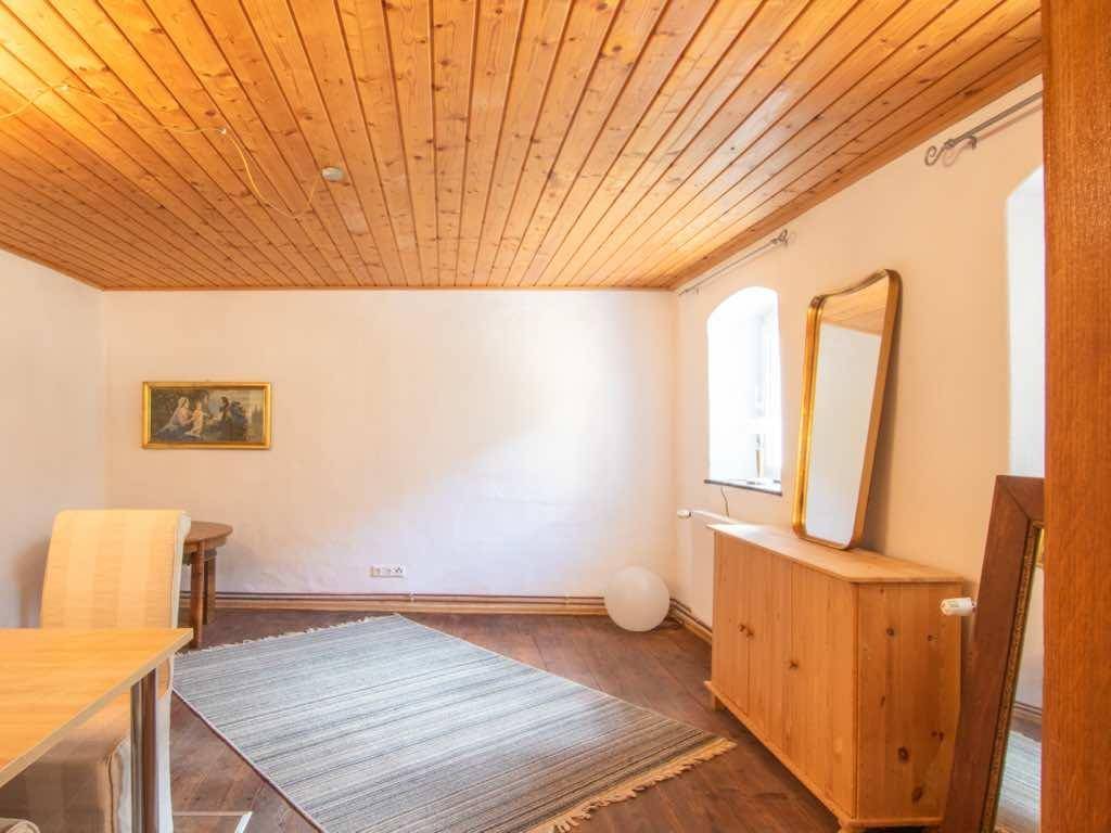Esszimmer mit Holzdecke, Teppich, Kommode und Spiegel, hell durch ein Fenster.