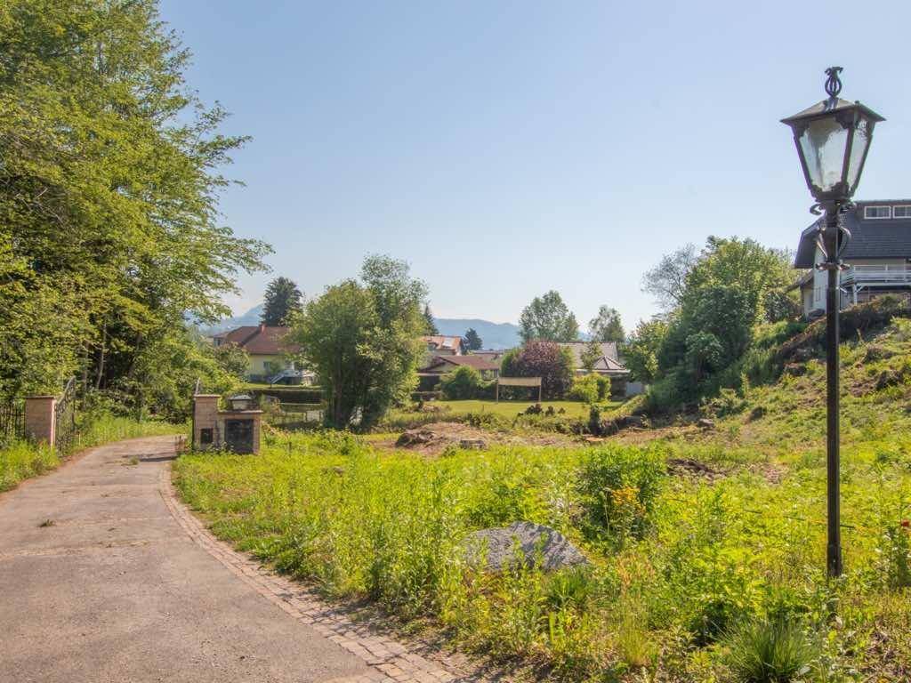 Unbebautes Grundstück mit einer historischen Straßenlaterne im Vordergrund und Blick auf Häuser und Berge.