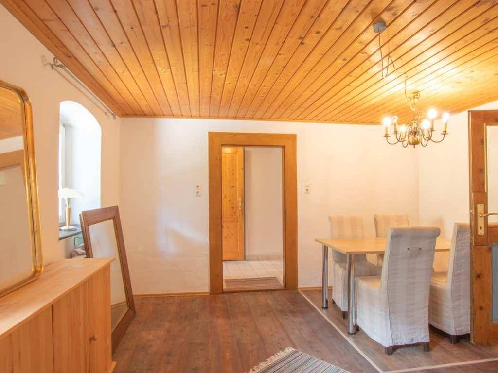 Esszimmer mit Holztisch, Stühlen und Kronleuchter, unter einer rustikalen Holzdecke.