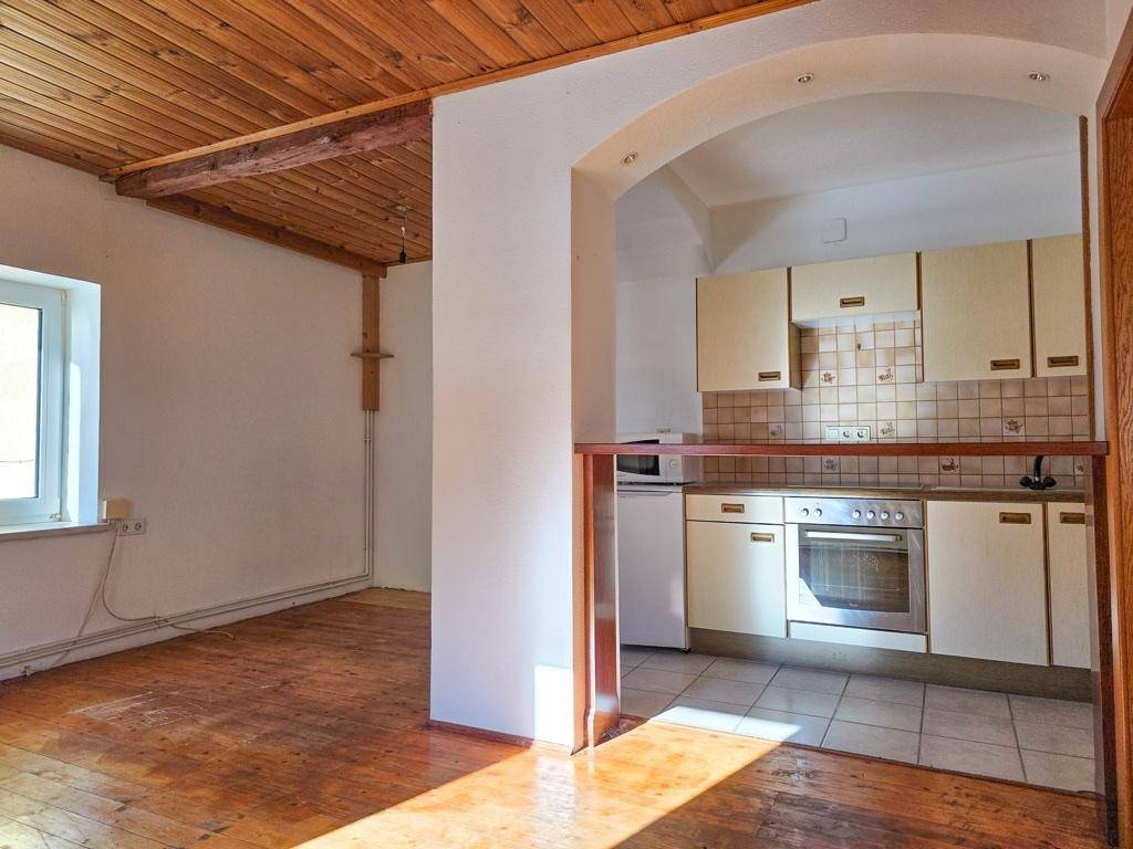 Offener Wohnbereich mit kleiner Küche, Holzboden und Holzdecke, hell und funktional.