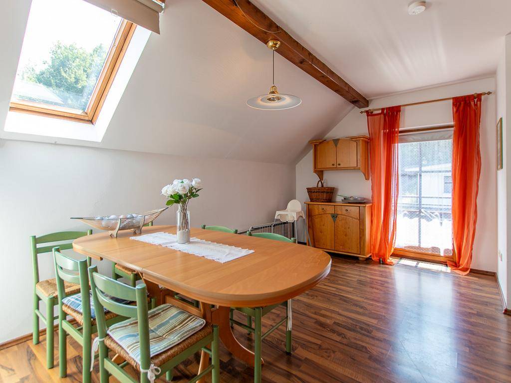 Heller Essbereich mit Holztisch, Dachfenster und Zugang zu einem kleinen Balkon, umgeben von Natur.