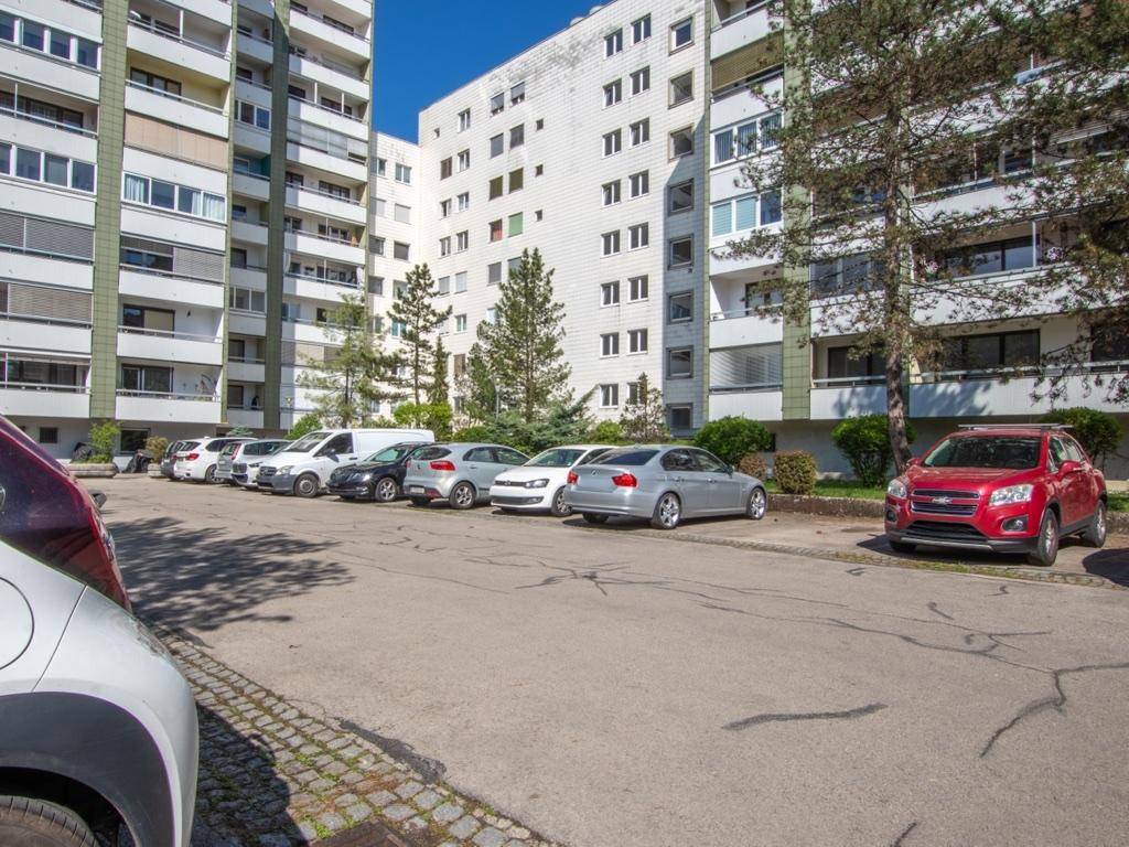 Außenansicht des Wohnkomplexes mit Parkplätzen und Bäumen.