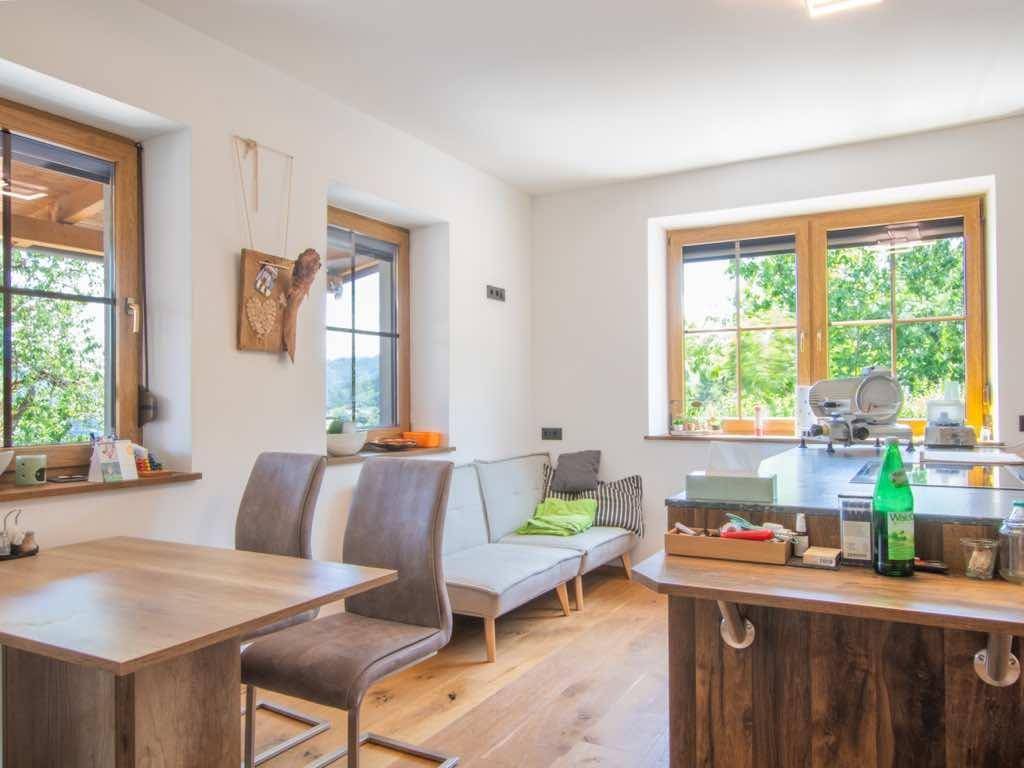 Heller Wohn- und Essbereich mit Holzboden, kleiner Sitzecke und Blick auf die grüne Umgebung.