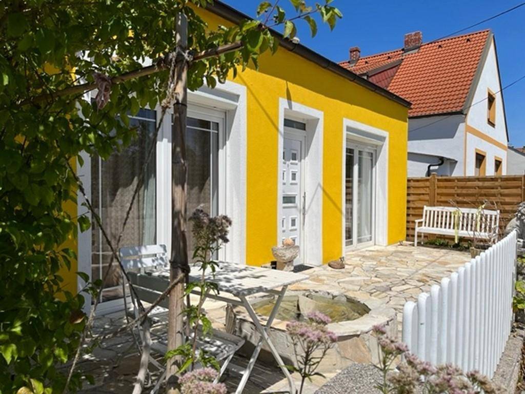 Seitlicher Terrassenbereich mit Steinplatten, einem kleinen Brunnen und weißem Gartenzaun.