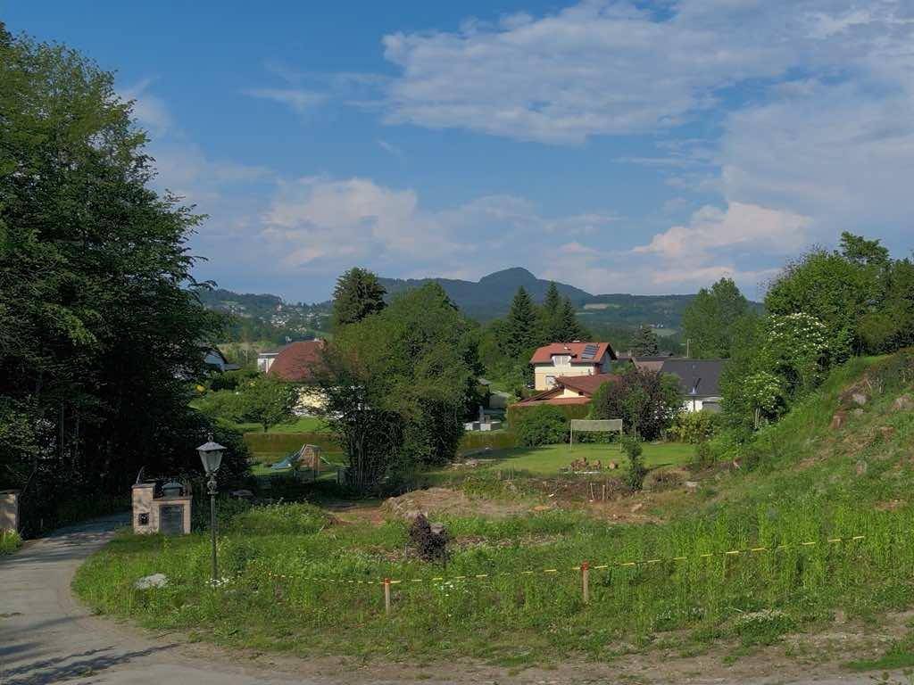 Unbebautes Grundstück mit grüner Wiese, umgeben von Häusern, Bäumen und einer malerischen Bergkulisse.