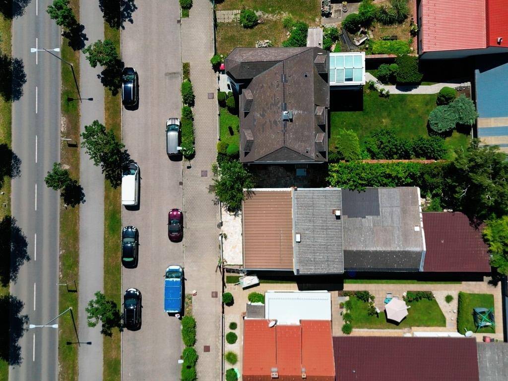 Vogelperspektive einer Wohnstraße mit Häusern, Gärten und parkenden Autos.