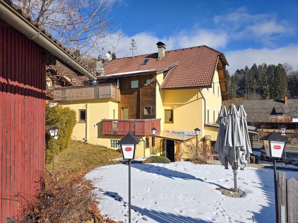 Rückansicht des gelben Gebäudes mit Balkonen, schneebedecktem Gartenbereich und umliegender Natur.