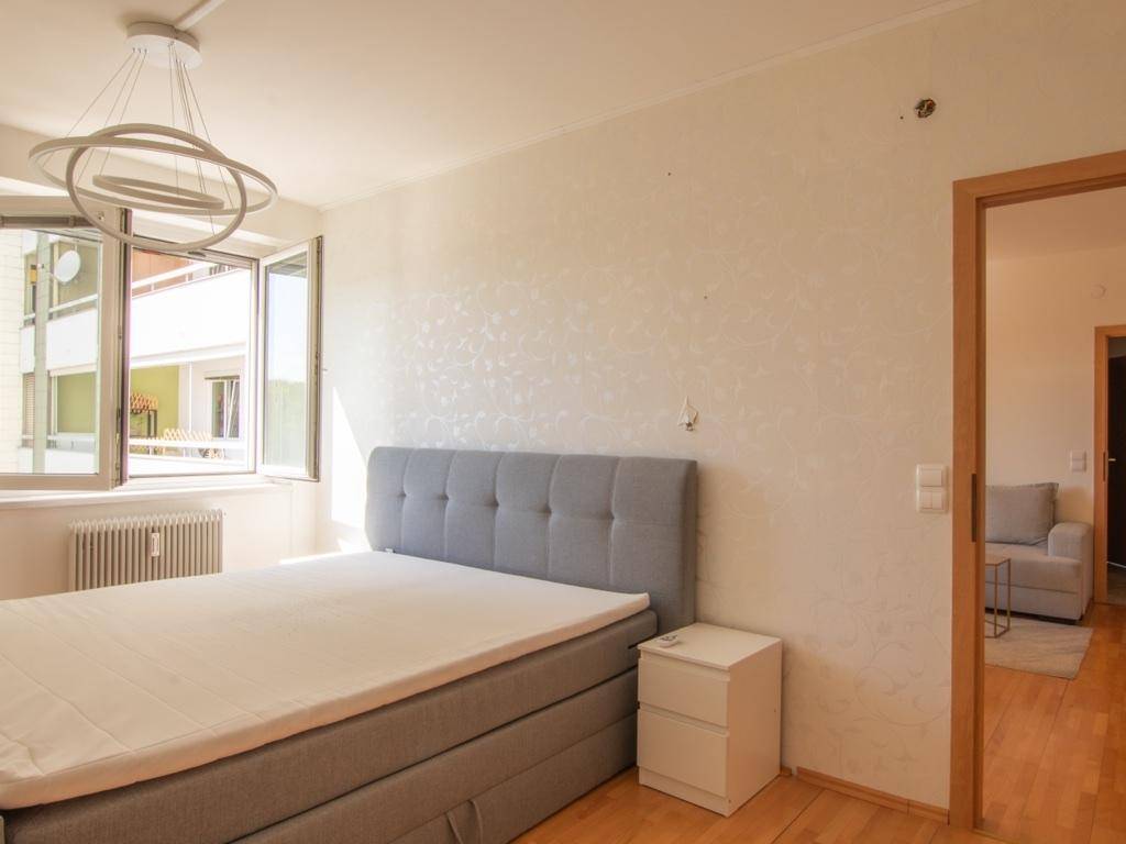 Helles Schlafzimmer mit Doppelbett, Nachttisch und Fenster mit Blick nach draußen.