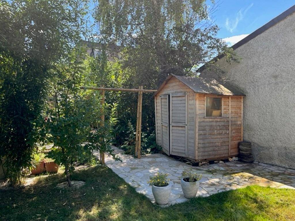 Gartenbereich mit Steinplattenweg, Rasenfläche und einem kleinen Holzschuppen.