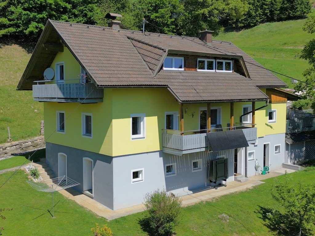 Zweistöckiges Haus mit gelb-grauer Fassade, braunem Ziegeldach und mehreren Balkonen.