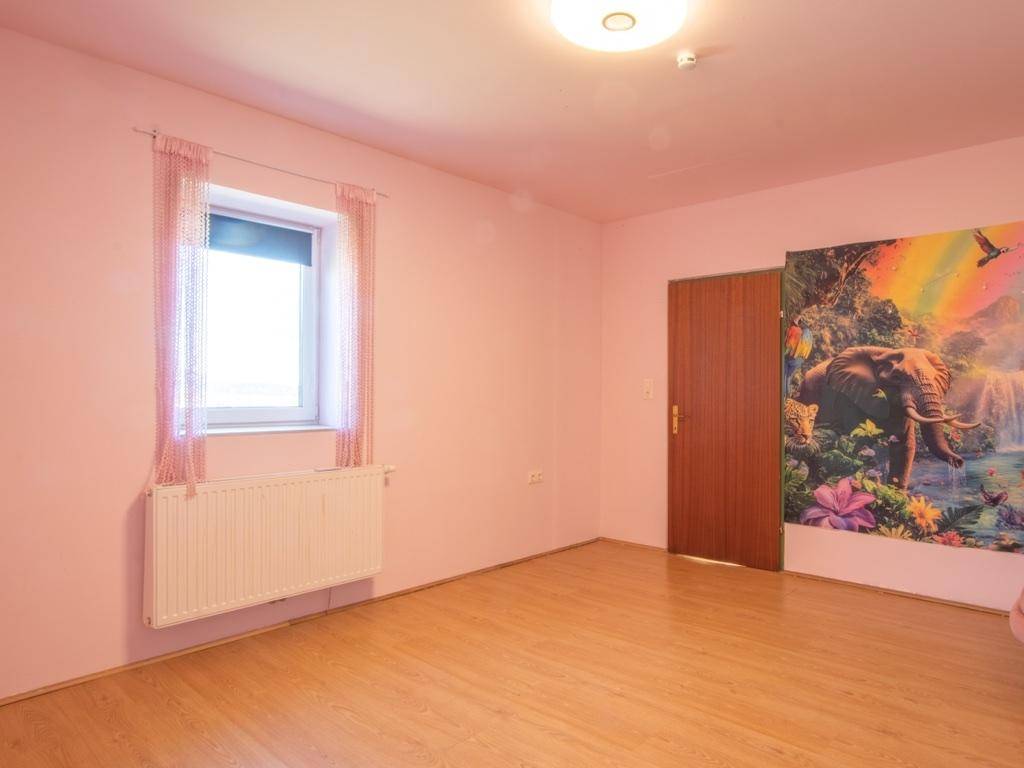 Kinderzimmer mit rosa Wänden, Laminatboden, Fenster und einem farbenfrohen Wandbild.