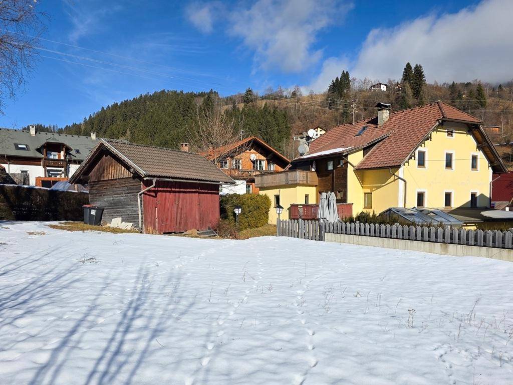 Gesamtansicht des Anwesens mit Nebengebäude, schneebedecktem Grundstück und Bergkulisse.