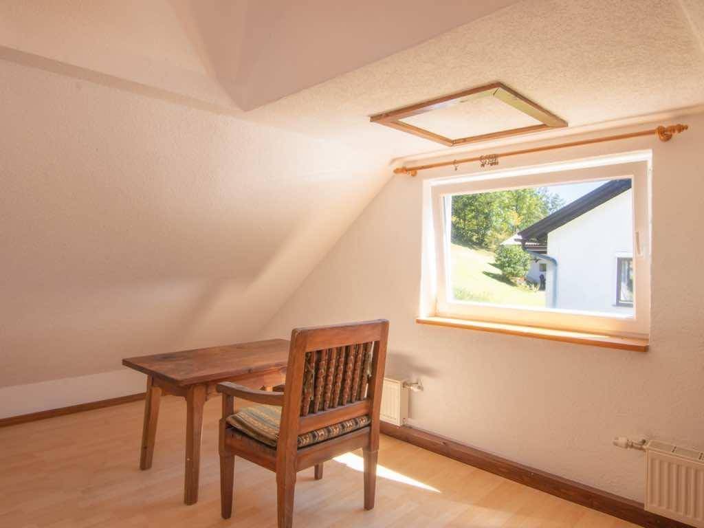 Helles Arbeitszimmer im Dachgeschoss mit Holzboden und Blick ins Grüne durch das Fenster.