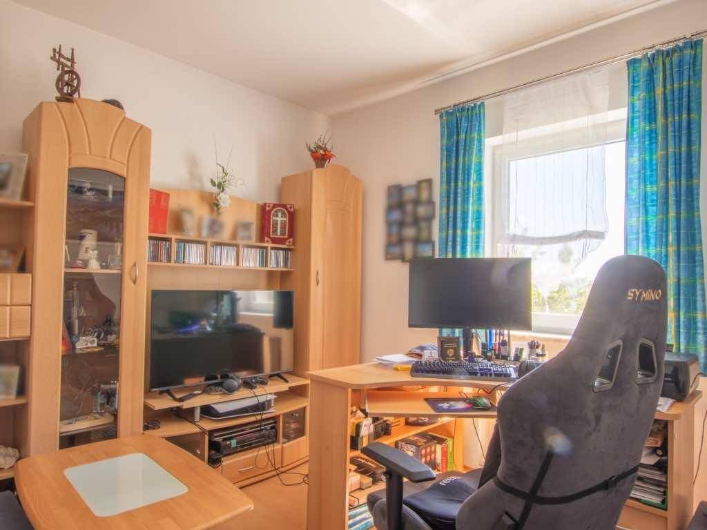 Helles Zimmer mit Schreibtisch, Gaming-Stuhl und Holzmöbeln, Blick ins Grüne.