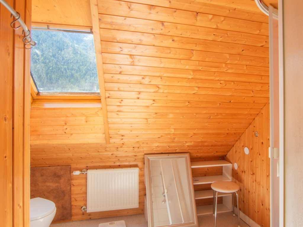 Badezimmer im Dachgeschoss mit Holzwänden, Toilette, Heizkörper und einem Dachfenster.