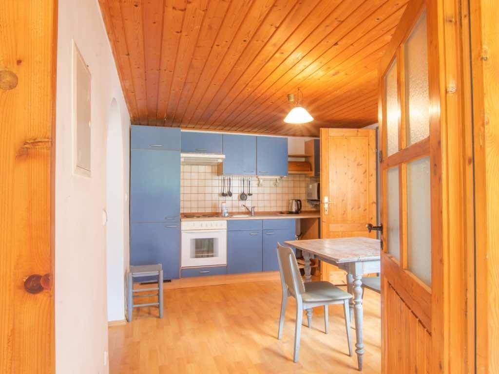 Küche mit blauen Schränken, Herd und einem kleinen Essbereich unter einer Holzdecke.