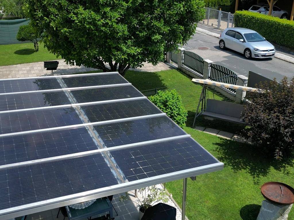 Draufsicht auf die überdachte Terrasse mit Solaranlage, Garten und angrenzender Straße.