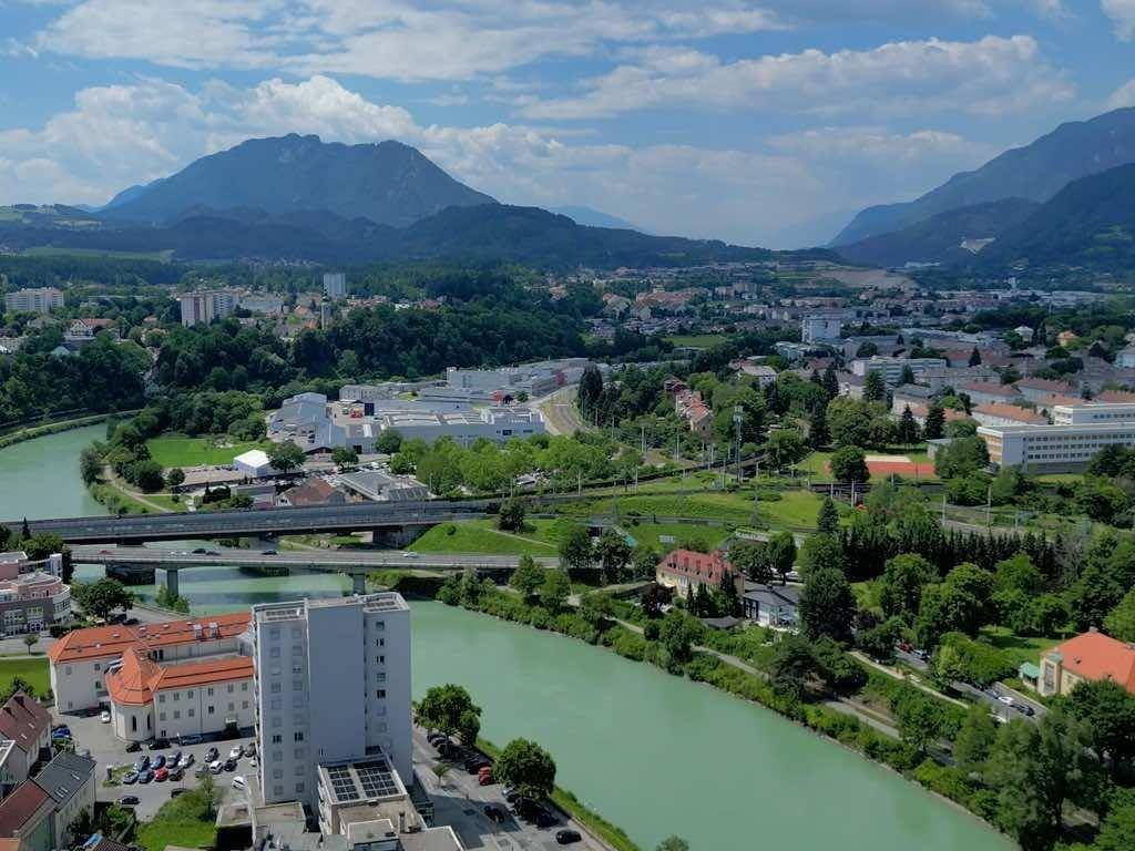 Panoramablick über die Stadt mit Fluss, Brücken, viel Grün und einer beeindruckenden Berglandschaft.