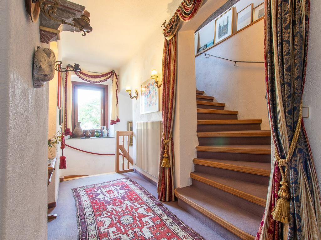 Traditioneller Flur mit Holztreppe, dekorativen Vorhängen und einem Fenster für natürliches Licht.