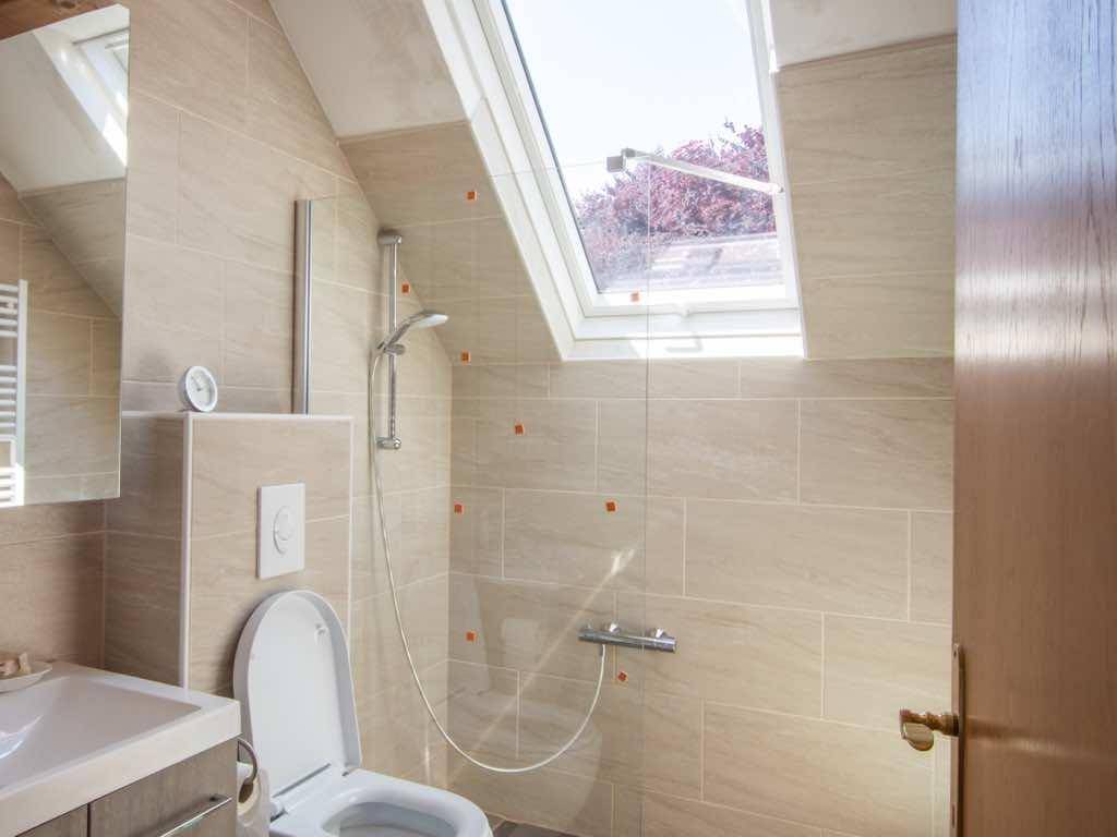 Helles Badezimmer mit WC, Waschbecken, Dusche und Dachfenster für Tageslicht.