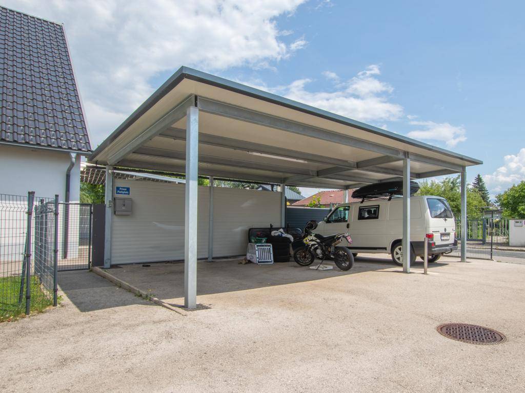 Geräumiger Carport mit Metallkonstruktion bietet Platz für mehrere Fahrzeuge und Fahrräder.