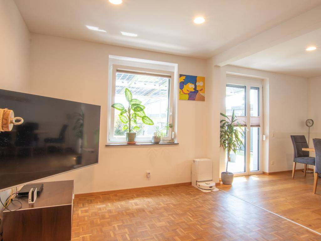 Helles Wohnzimmer mit Parkettboden, Fenster und Zugang zur Terrasse oder zum Garten.