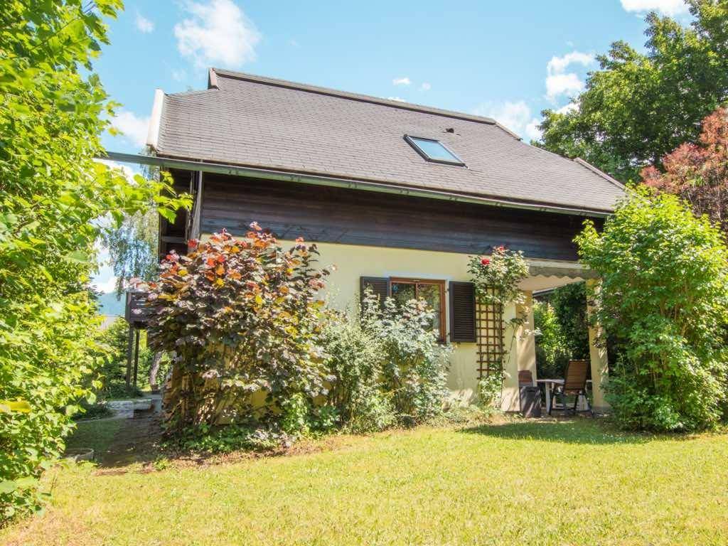 Seitlicher Blick auf das Haus mit kleiner Terrasse und Gartenmöbeln, umgeben von viel Grün.