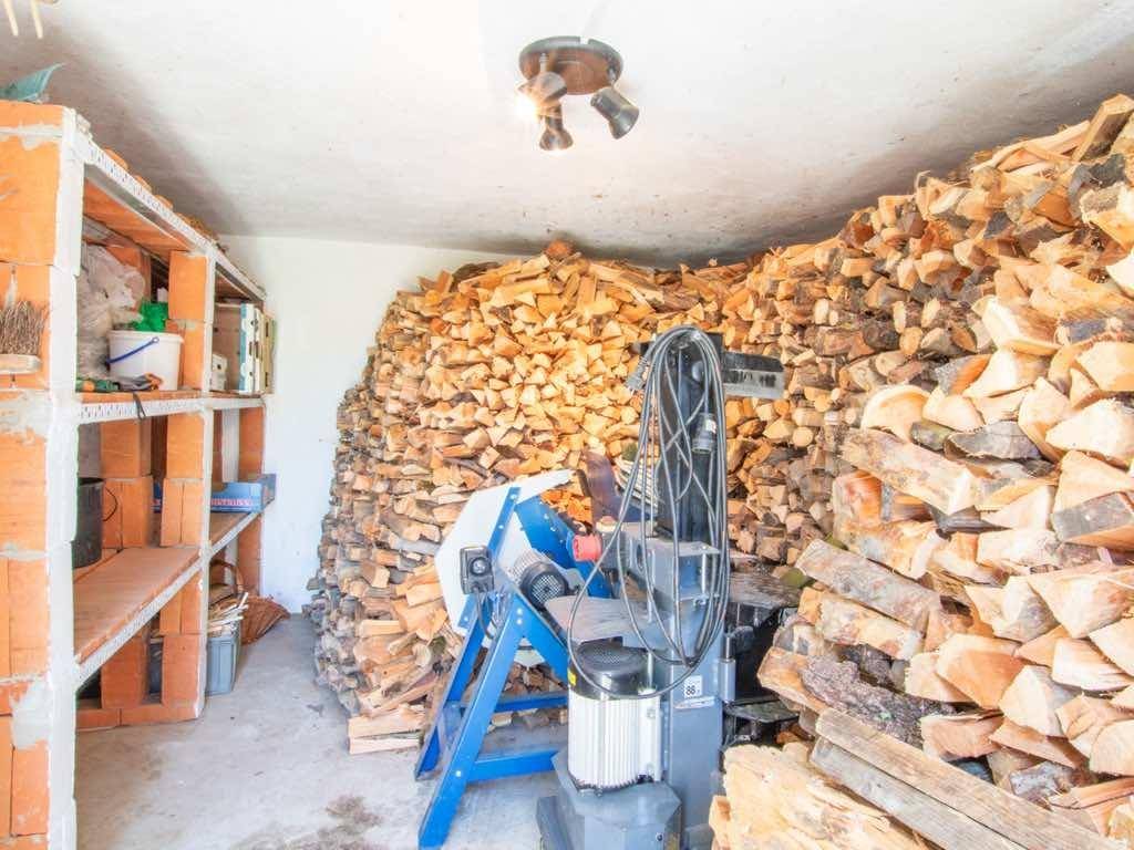 Lagerraum mit gestapeltem Brennholz und einer Holzspaltmaschine, funktional eingerichtet.