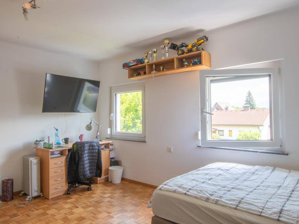 Schlafzimmer mit Schreibtisch, Fenstern und Blick ins Grüne.