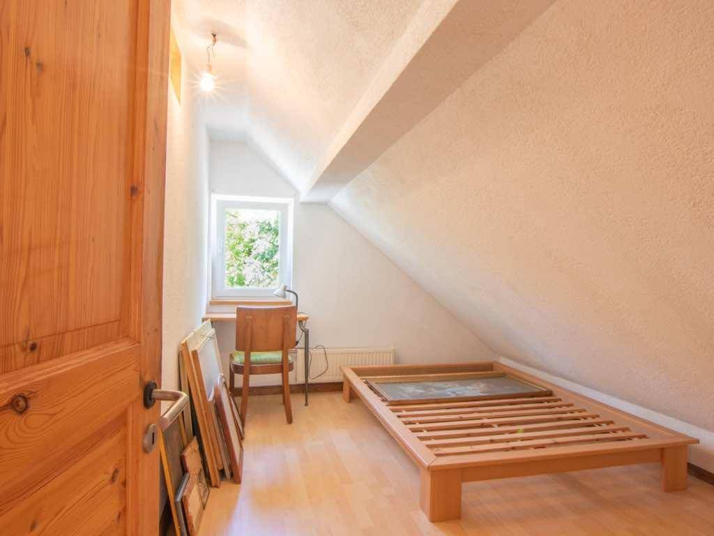 Helles Schlafzimmer im Dachgeschoss mit Holzboden, Einzelbett und einem Fenster mit Blick ins Grüne.