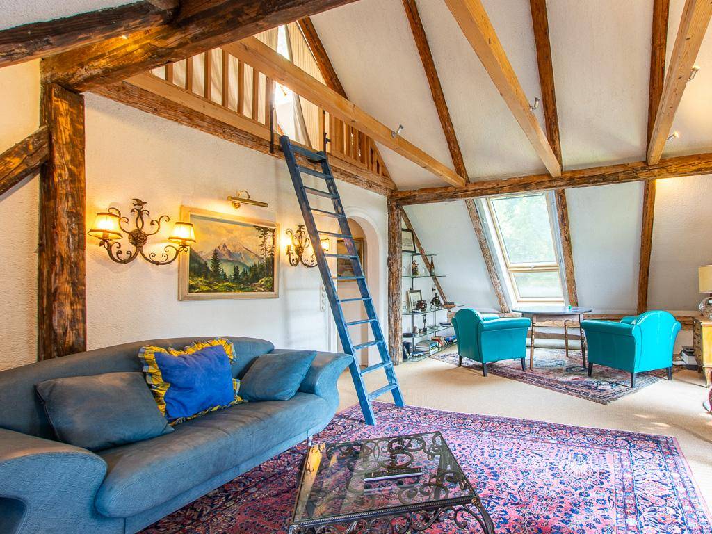 Gemütlicher Wohnbereich im Dachgeschoss mit sichtbaren Holzbalken, Dachfenstern und einer Leiter zum Loft.