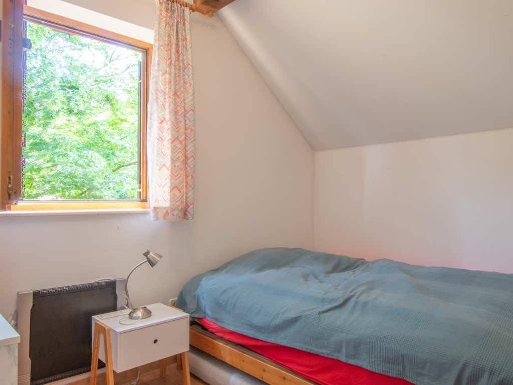 Kleines Schlafzimmer mit Einzelbett und Fenster, das viel Grün hereinlässt.