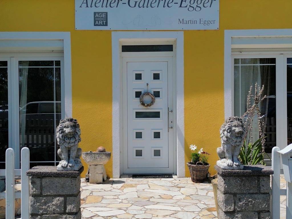 Nahaufnahme des Hauseingangs mit weißer Tür, Steinlöwen und einem Kranz an der Tür.