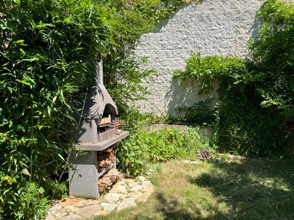 Grüner Gartenbereich mit Rasenfläche und einem gemauerten Grillplatz.