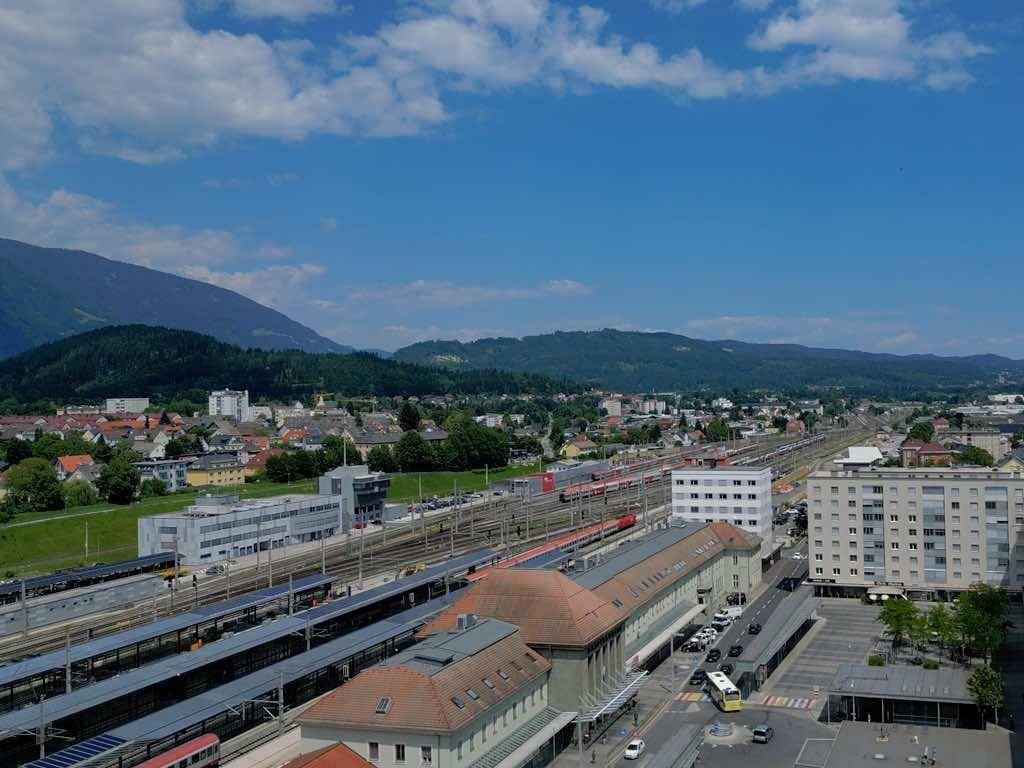 Luftaufnahme der Stadt mit großem Bahnhof, Gleisen und Gebäuden vor einer Bergkulisse.