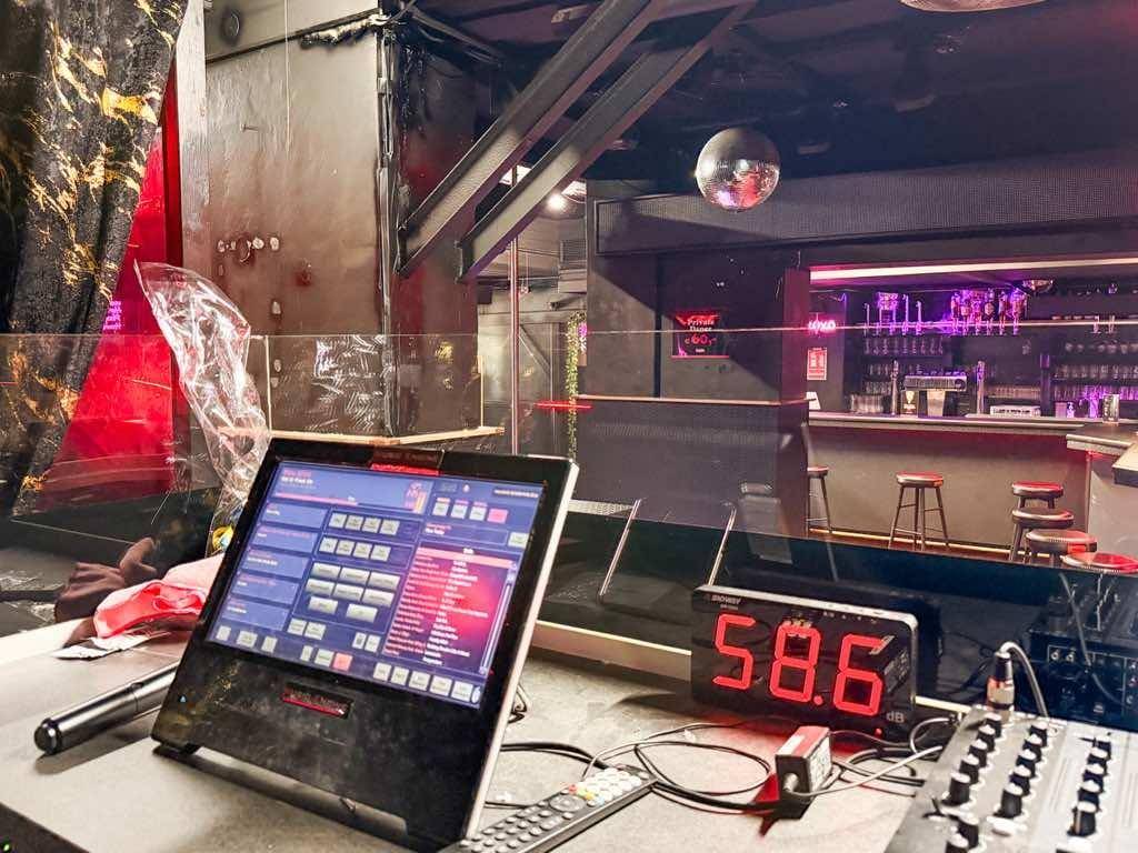 DJ-Pult mit Bildschirmen und Mischpult, umgeben von der Bar und Tanzfläche.