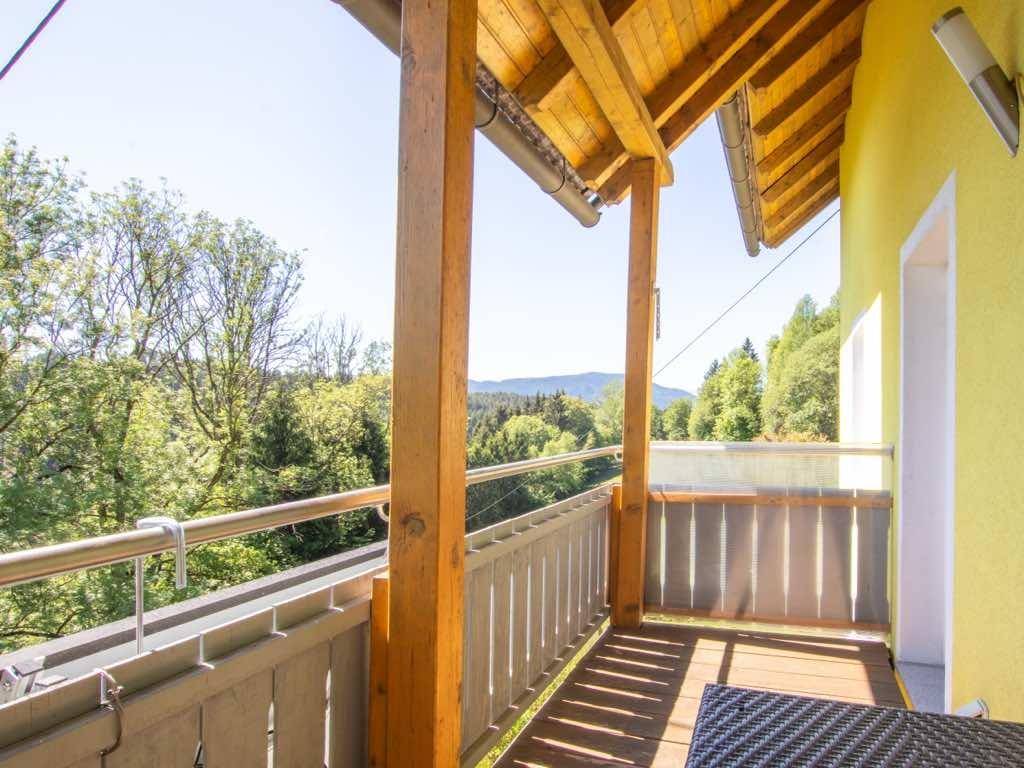 Sonniger Balkon mit Holzbalken und Geländer, bietet einen weiten Blick ins Grüne.