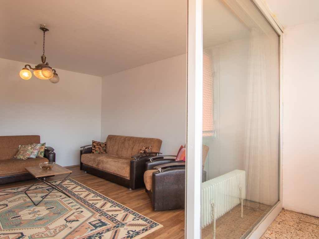 Heller Wohnbereich mit Holzboden und großzügiger Glasfront zum Balkon, die viel Licht hereinlässt.