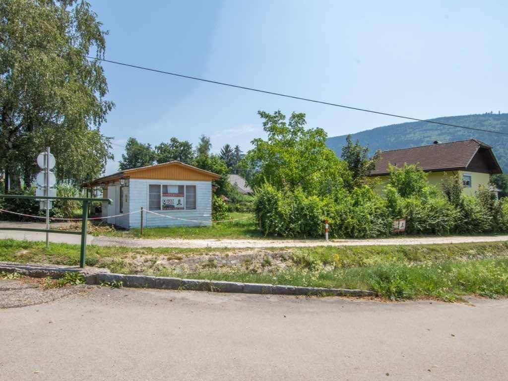 Kleines Gebäude mit Verkaufsschild an einer Straße, umgeben von grüner Landschaft.