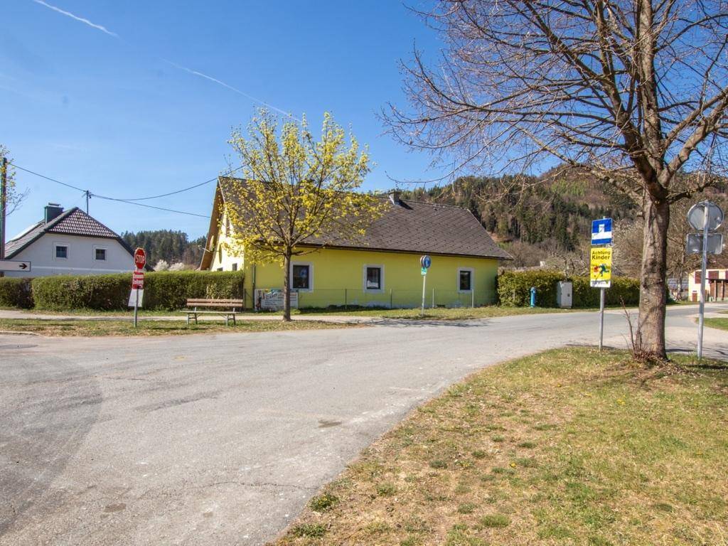 Straßenansicht des gelben Hauses in ländlicher Umgebung mit Sitzbank und Verkehrsschildern.