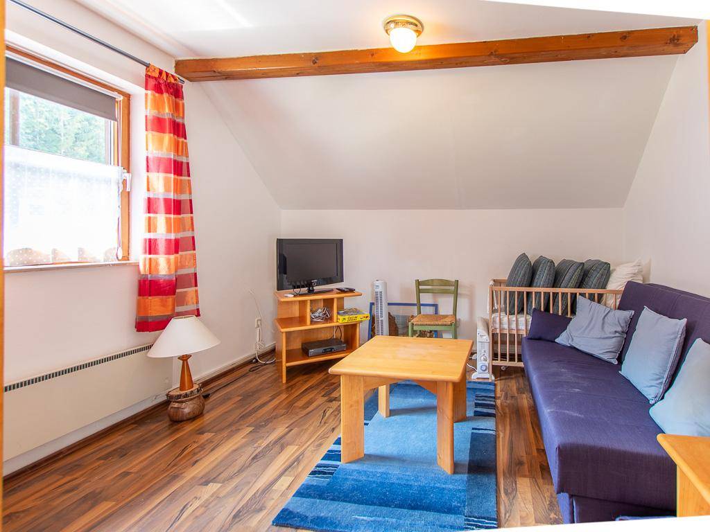 Gemütliches Wohnzimmer unter dem Dach mit Sofa, Fernseher, Holzboden und farbigen Akzenten.