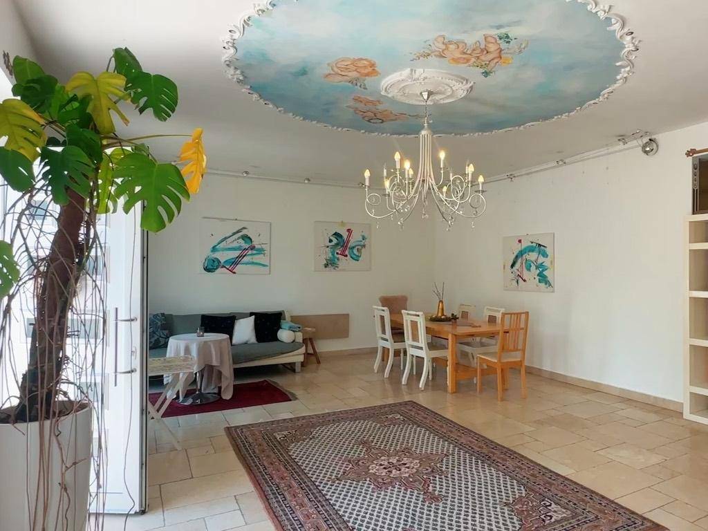 Heller Wohn- und Essbereich mit großem Teppich, Kronleuchter und kunstvoller Deckenmalerei.
