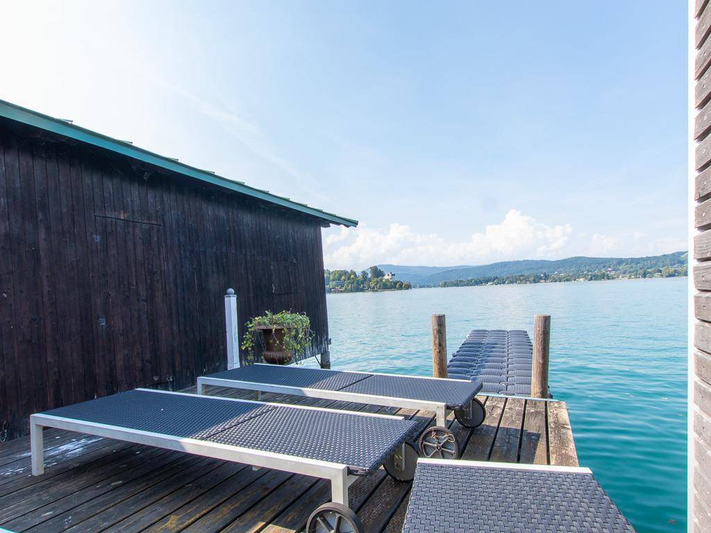 Holzterrasse am See mit Sonnenliegen und unverbautem Blick auf das klare Wasser und die Landschaft.