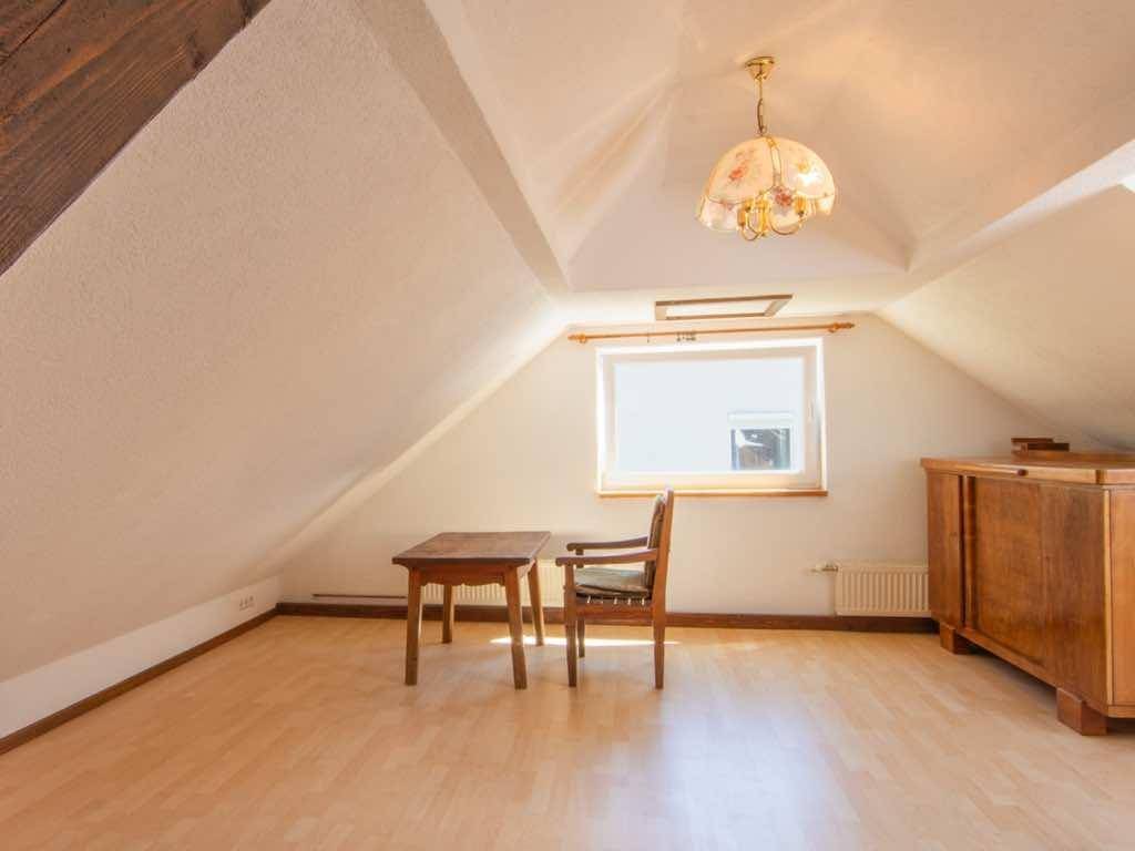 Helles Wohnzimmer im Dachgeschoss mit Holzboden, sichtbaren Balken und traditioneller Einrichtung.