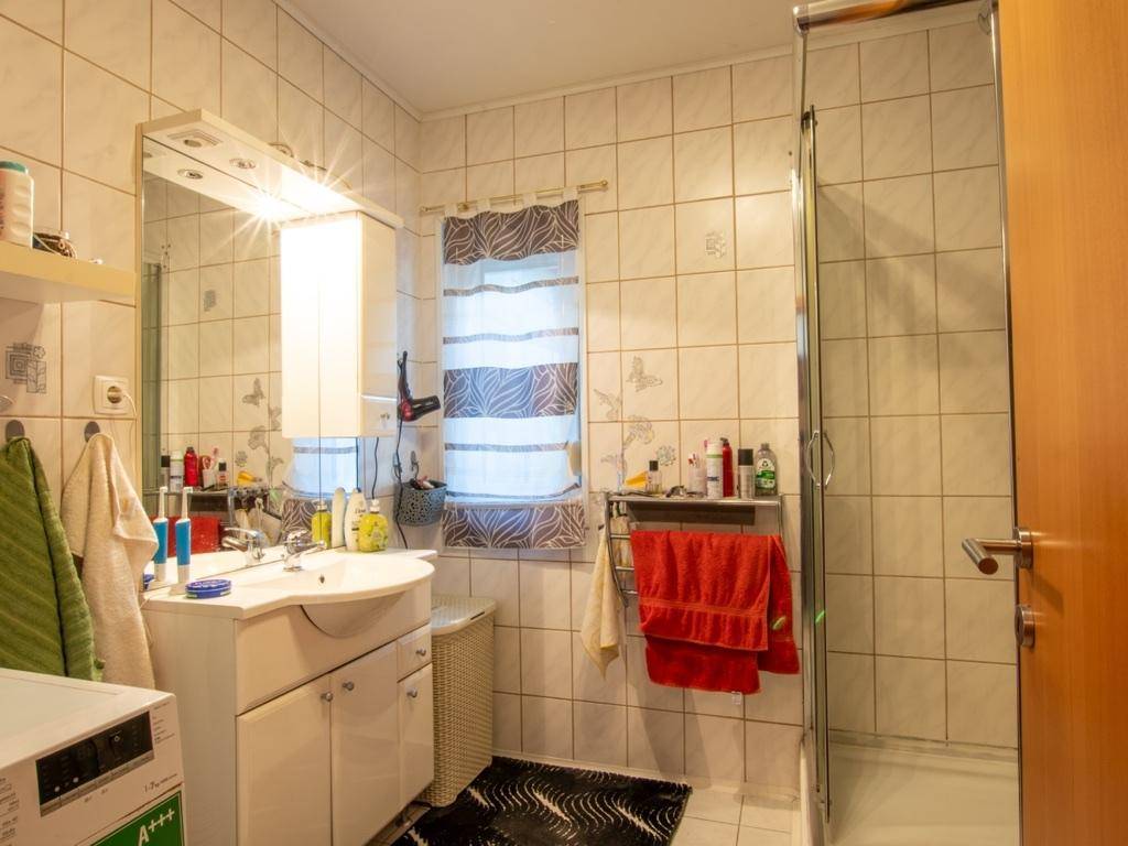 Gefliestes Badezimmer mit Duschkabine, Waschbecken und Spiegelschrank.
