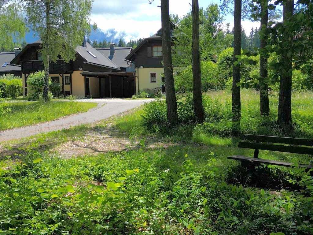 Haus in ländlicher Umgebung mit Bäumen, Wiesen und einer Holzbank im Vordergrund.